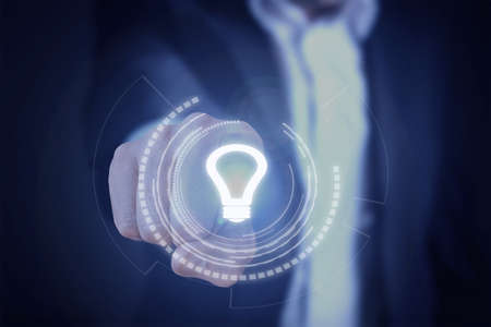 Man in suit presses virtual, hologram light bulb button. New idea, innovation, invention technology conceptの写真素材