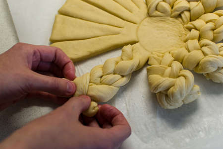 Female hands braiding dough on white working kitchen table, close up