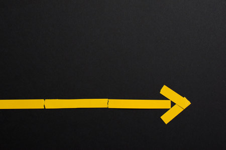 Yellow arrow made of paper on black background with copy space