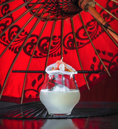Coconut milk with ice cubes on black table and red umbrellaの写真素材