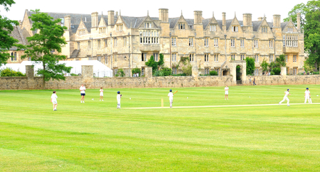 OXFORD, ENGLAND - JULY 8, 2014: Children play cricket outdoors in front of old university building...