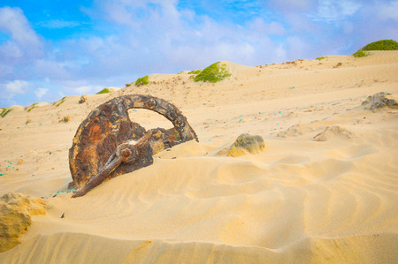 View of desert landscape with dunes and rusty wheelの写真素材