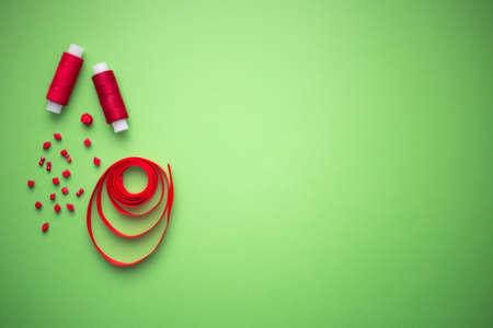 Red threads, red beads and red ribbon on a green background with copyspace