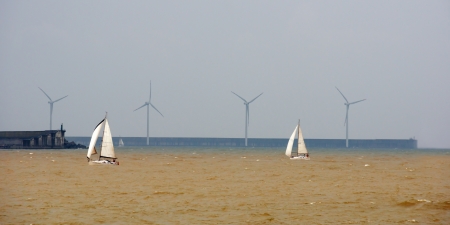 Sailboats in rough sea and a wind farmの写真素材