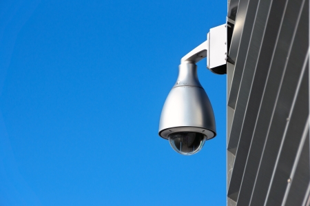 surveillance security camera on wall against blue sky