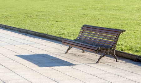 wooden bench in park near the grass on sunny dayの写真素材