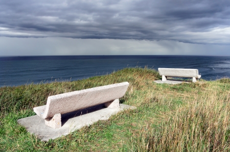 stone benches on cliff near the sea with stormy cloudsの写真素材