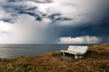 bench on cliff with storm over the seaの写真素材