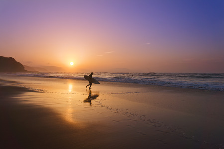surfer entering water at the sunsetの写真素材