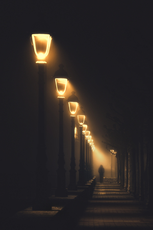 person walking on dark street illuminated with streetlampsの写真素材