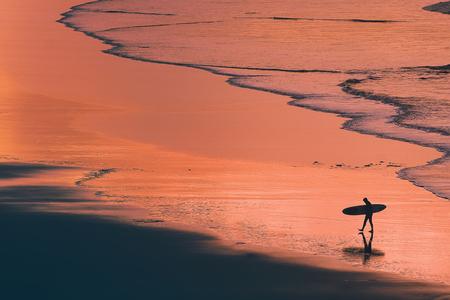 distant surfer silhouette in the shore at the sunsetの写真素材