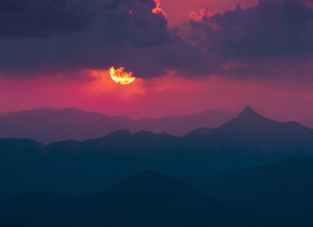 dark background with sun and clouds over far mountains at sunsetの写真素材