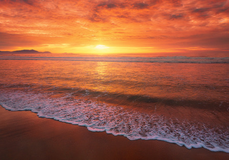 beautiful red sunset on beach with a wave on the shoreの写真素材