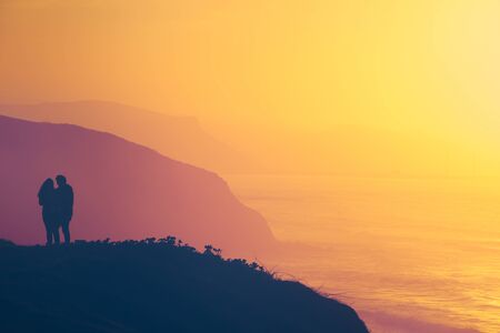 romantic scene of a couple on cliff watching the sea