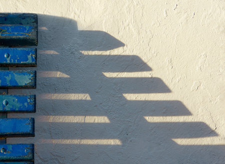 old wooden bench against white wall with shadowの写真素材