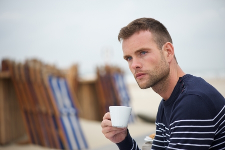 young guy relaxing at the beach and drinking his coffeeの写真素材