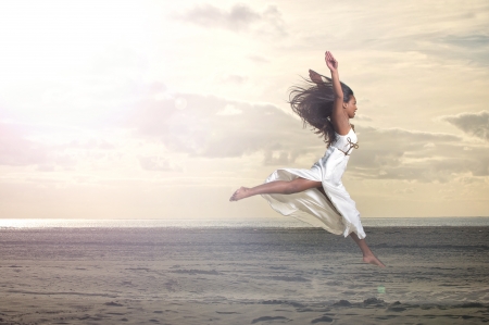 An african girl jumping in a white dress at the beachの写真素材