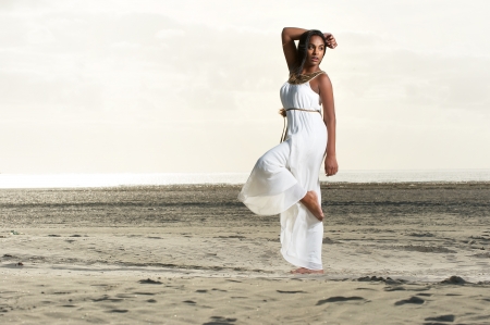 Beautiful african american girl  in a white dress doing a dance pose at the beachの写真素材