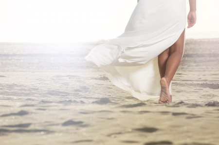 An African American girl is walking on the sand with a flowing white dress. の写真素材
