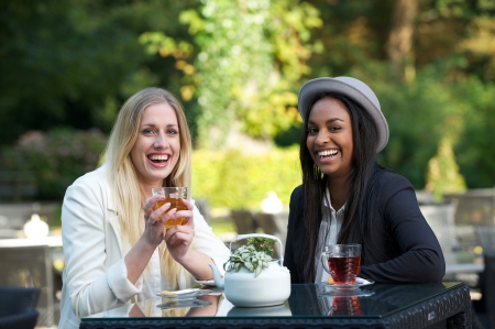 two girls drinking tea and smiling outdoorsの写真素材