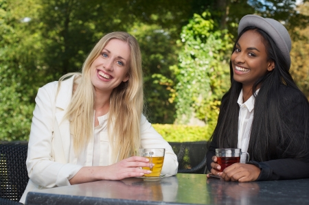 Two Girls Sitting at an Outdoors Cafe Smiling and Having Teaの写真素材