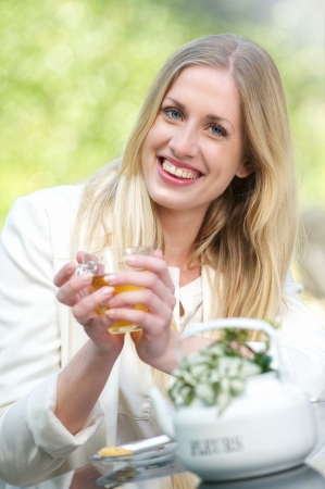 A young blonde girl is holding a cup of tea outdoors の写真素材