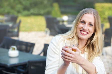 A blonde girl is looking away and smiling with a cup of tea in her handの写真素材