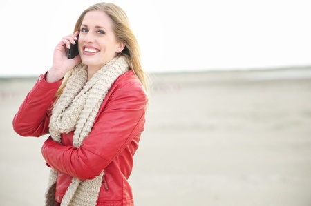 Smiling Blond Girl on her Mobile Phone at the Beachの写真素材