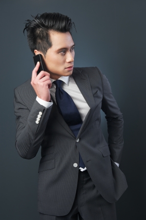 Asian businessman posing with mobile phone. Photographed against a grey background.の写真素材