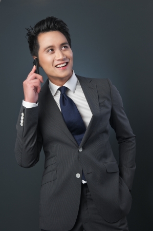 Asian businessman on the phone and smiling in the studio. Photographed against a gray background.の写真素材