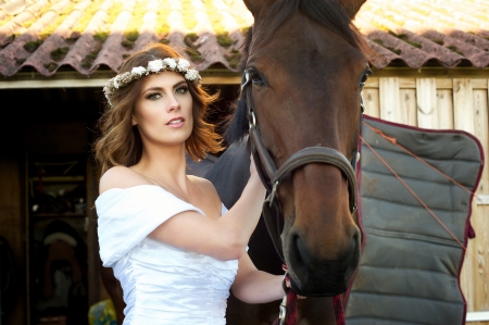 Alluring bride wearing a white wedding dress and flowers in her hair, standing next to a horseの写真素材