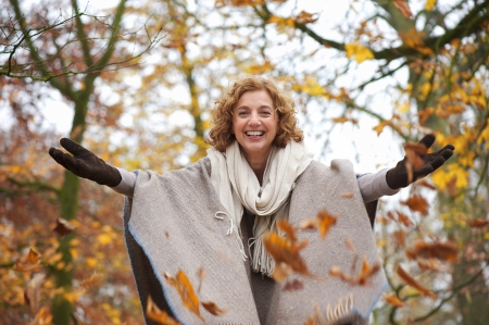 Middle aged woman throwing leaves in autumn with open armsの写真素材