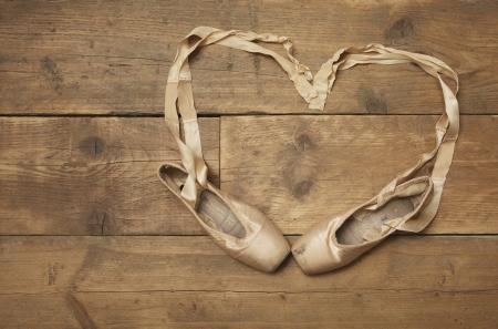 Two ballet shoes on wooden floor with ribbon in heart shape - above viewの写真素材