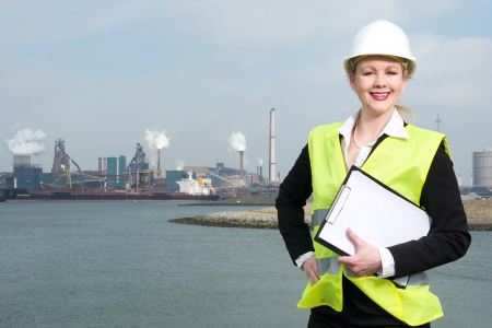 Portrait of a happy businesswoman in hardhat and safety vest standing outdoors with clipboardの写真素材