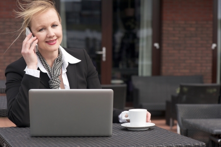 Portrait of a businesswoman on phone outdoors with laptop and cup of coffeeの写真素材