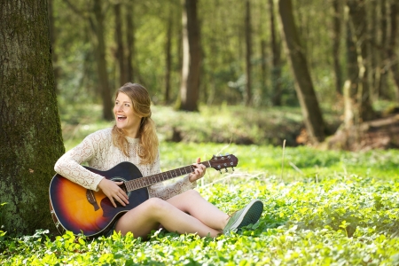 Portrait of a beautiful young woman smiling and playing guitar in the forestの写真素材