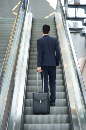 Business man going up escalator holding travel bag - rear viewの写真素材
