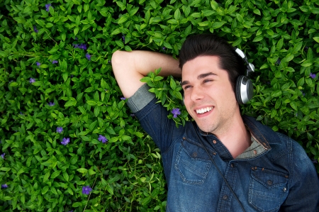 Portrait of a happy young man lying on grass, listening to music with headphones