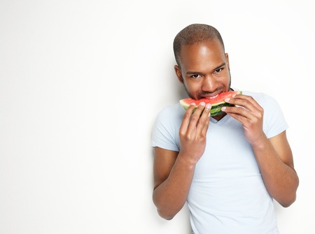 Portrait of a happy young black man eating watermelon against white backgroundの写真素材