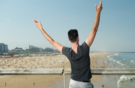 Portrait of a young man with hands raised overlooking beach with peopleの写真素材