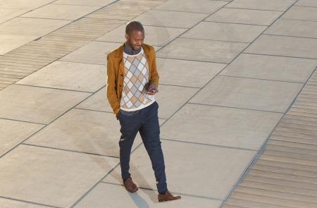 Portrait of a happy young man walking and sending message on mobile phoneの写真素材