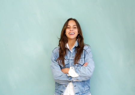 Horizontal portrait of a young woman laughing with arms crossed in relaxed pose against blue...