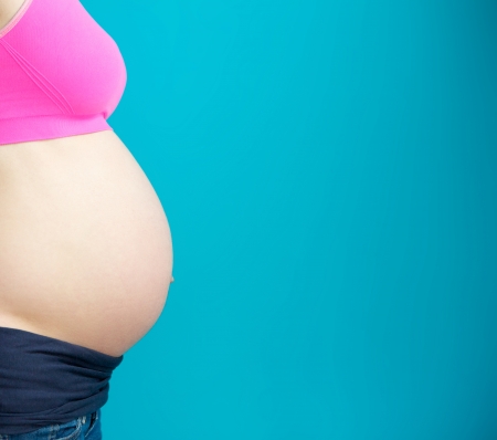 Side view close up pregnant woman stomach on blue background - copy space 