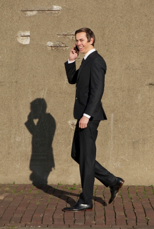 Full length portrait of a smiling businessman walking and talking on cellphoneの写真素材