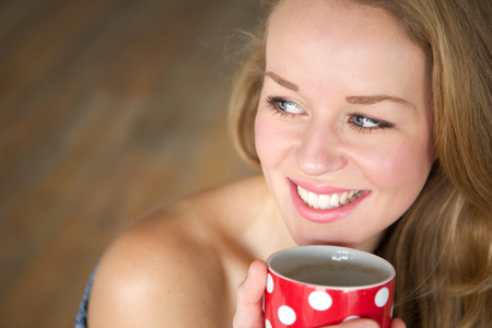 Close up portrait of a young woman smiling and  enjoying a cup of tea at homeの写真素材
