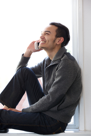 Portrait of a young man relaxing and on mobile phone at homeの写真素材