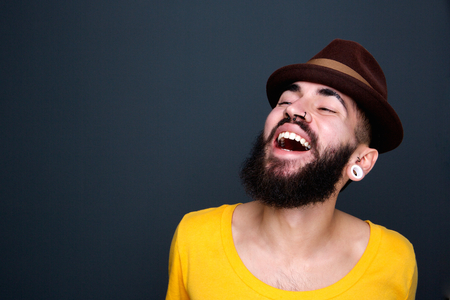 Close up portrait of a handsome young man with beard and hat laughing on gray backgroundの写真素材