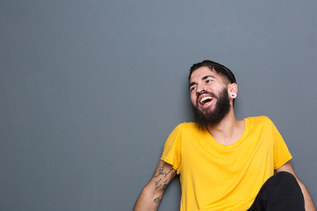 Portrait of handsome young man sitting against gray background laughing の写真素材