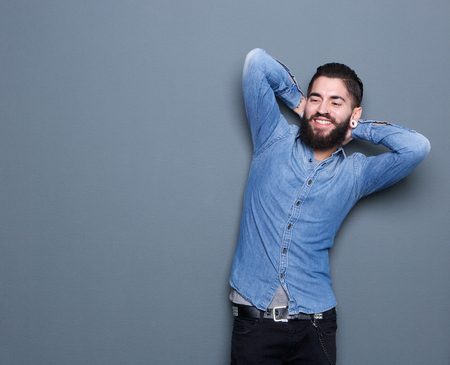 Portrait of a handsome young man with beard relaxing with hands behind head on gray backgroundの写真素材