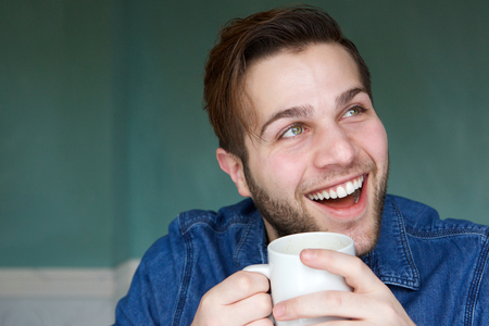 Close up portrait of a young man smiling with cup of coffeeの写真素材